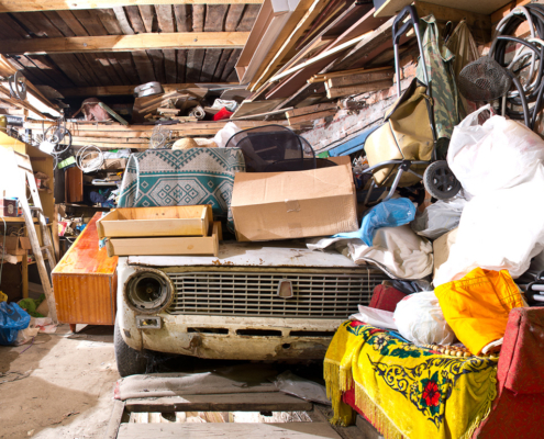 Roll Off Dumpster- Junk Removal- Garage inside. Old broken car, shelves with tools and stacks of things.